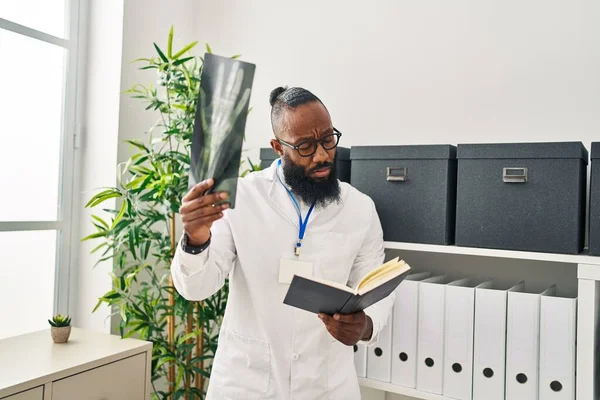 Joven Afroamericano Hombre Vistiendo Doctor Uniforme Lectura Libro Buscando Xray — Foto de Stock