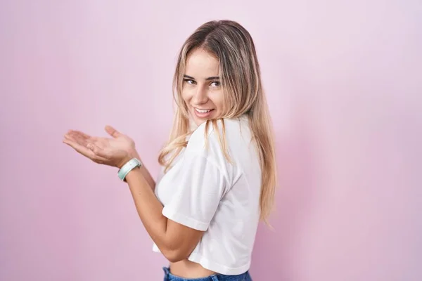 Young Blonde Woman Standing Pink Background Pointing Aside Hands Open — Zdjęcie stockowe