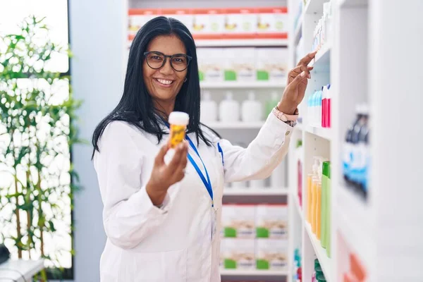 Middelbare Leeftijd Spaanse Vrouw Apotheker Holding Pillen Fles Plank Bij — Stockfoto