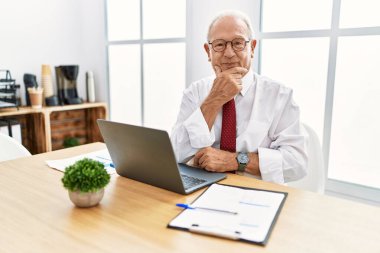 Ofiste çalışan son sınıf öğrencisi bilgisayarla kameraya bakıyor kollarını kavuşturup gülümsüyor ve çenesini kaldırıyor. Olumlu düşünmek. 