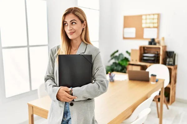 Blonde business woman at the office smiling looking to the side and staring away thinking.