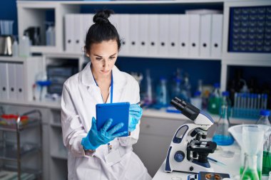 Young caucasian woman scientist using touchpad with relaxed expression at laboratory