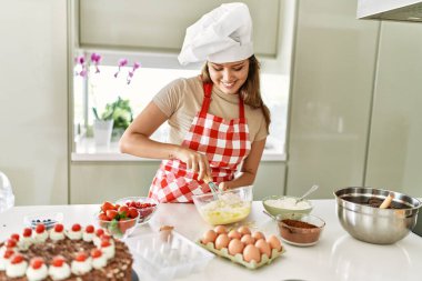 Genç, güzel İspanyol kadın, gülümsüyor. Mutfakta yumurta karıştırıyor.