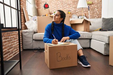 Young hispanic woman smiling confident writing on book at new home
