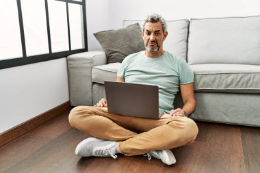 Orta yaşlı İspanyol bir adam oturma odasında dizüstü bilgisayar kullanıyor. Depresyonda ve endişe içinde, sinirli ve korkmuş bir şekilde oturuyor. hüzünlü ifade. 