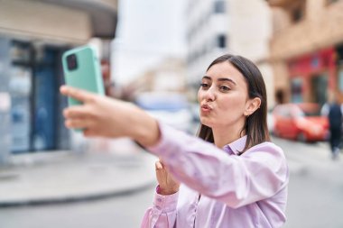 Genç İspanyol kadın gülümsüyor. Kendine güveni tam. Sokakta akıllı telefonun yanında selfie çekiyor.