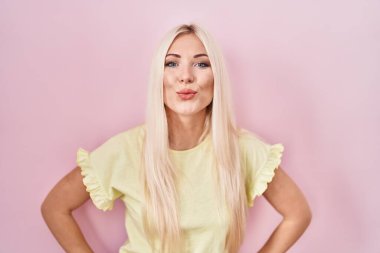 Caucasian woman standing over pink background looking at the camera blowing a kiss on air being lovely and sexy. love expression. 