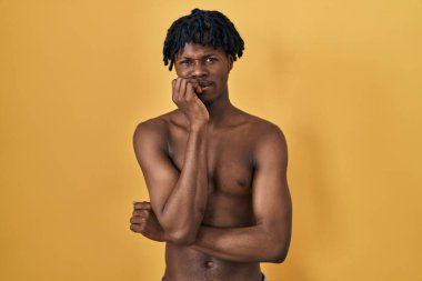 Young african man with dreadlocks standing shirtless looking stressed and nervous with hands on mouth biting nails. anxiety problem. 