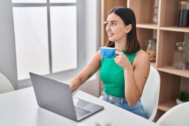 Young hispanic woman using laptop and drinking coffee at home