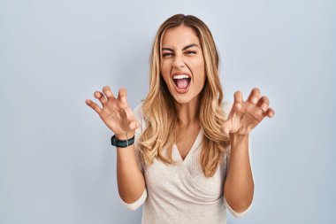 Soyutlanmış arka planda duran genç sarışın kadın gülüyor. Pençe hareketlerini kedi gibi yapıyor. Agresif ve seksi bir ifade. 