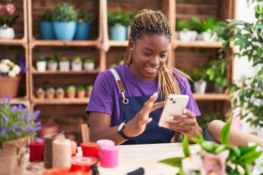Afrikalı Amerikalı kadın çiçekçi çiçekçiye akıllı telefon kullanarak gülümsüyor.