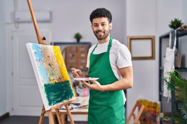 Genç Arap ressam, resim stüdyosunda kendine güvenen bir gülümseme.