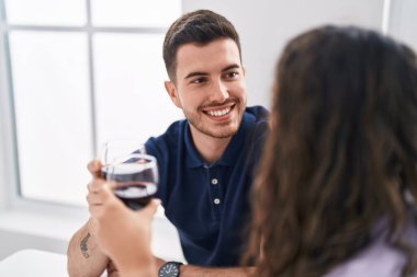 Young hispanic couple drinking wine sitting on table at home