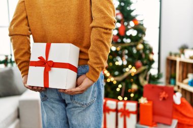 Evdeki Noel ağacının yanında duran bir adam hediyesini sırtında taşıyor..