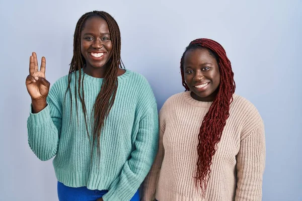Две Африканки Стоят Синем Фоне Показывают Пальцем Номер Три Улыбаясь — стоковое фото