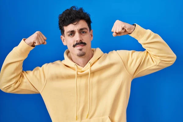 Hispanic Man Standing Blue Background Showing Arms Muscles Smiling Proud — Stockfoto