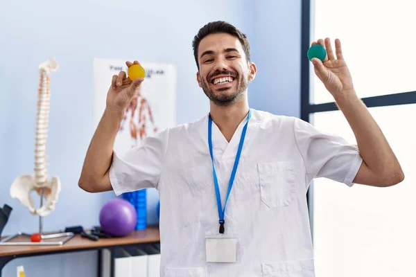 Young Hispanic Physiotherapist Man Holding Strength Balls Train Hand Muscles — Stockfoto