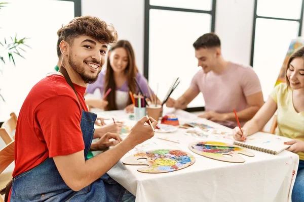 Group of people drawing sitting on the table. Young man smiling happy looking to the camera at art studio.