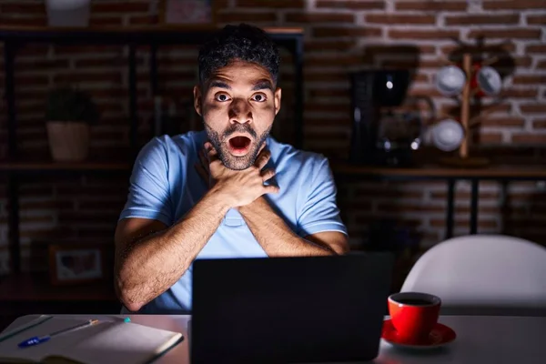 Hispanic man with beard using laptop at night shouting and suffocate because painful strangle. health problem. asphyxiate and suicide concept.