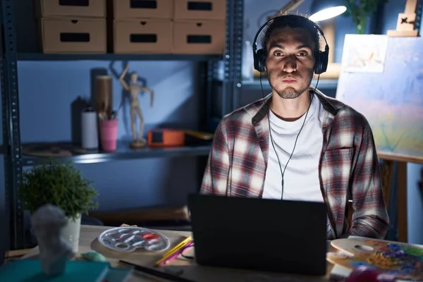 Young Hispanic Man Sitting Art Studio Laptop Late Night Puffing — Zdjęcie stockowe