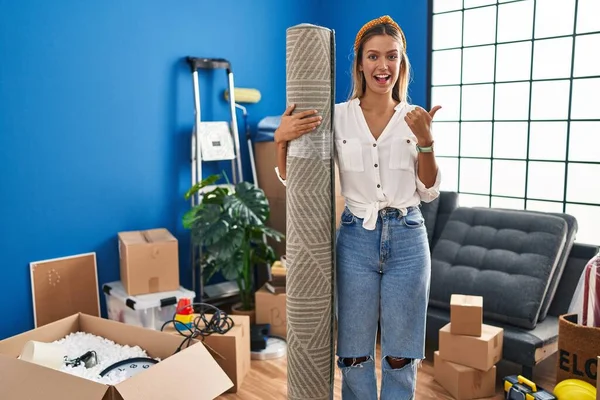 Young Blonde Woman Moving New Home Holding Rug Pointing Thumb — ストック写真