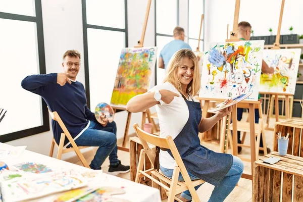 Group of middle age artist at art studio looking confident with smile on face, pointing oneself with fingers proud and happy.