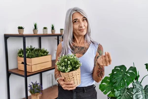手でお金のジェスチャーを行う家で緑の植物の鍋を保持する中世の白髪の女性 給与支払いを求めて 億万長者のビジネス — ストック写真