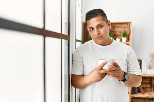 Young Hispanic Man Serious Expression Drinking Coffee Standing Home — Fotografia de Stock