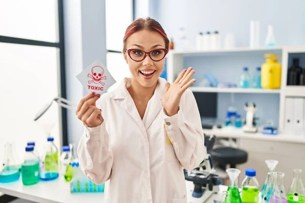 Joven Mujer Caucásica Trabajando Laboratorio Científico Sosteniendo Etiqueta Tóxica Celebrando —  Fotos de Stock