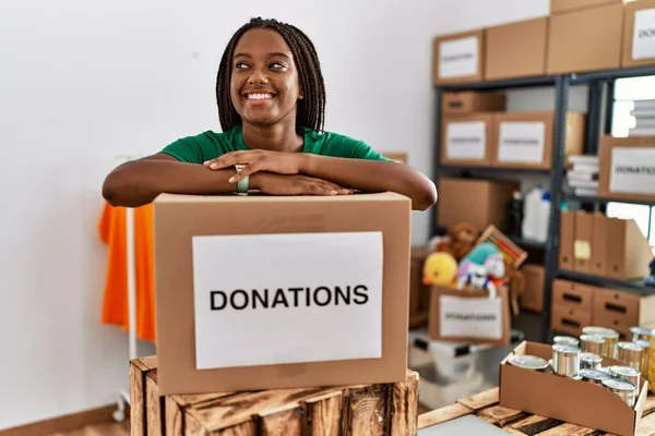 Young african american woman wearing volunteer uniform leaning on donations package at charity center