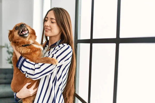 Genç Spanyol Kadın Gülümsüyor Kendine Güvenen Sarılan Köpek Evde Duruyor — Stok fotoğraf