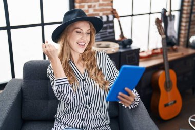 Müzik stüdyosundaki güzel sarışın kadın tablet kullanıyor gururla bağırıyor, zaferi kutluyor ve kollarını kaldırdığı için çok heyecanlı. 