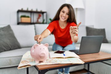 Genç esmer kadın domuzcuk kumbarasına para koyuyor seyahat için para biriktirip gülümsüyor mutlu bir şekilde elini ve parmağını yana uzatıyordu. 