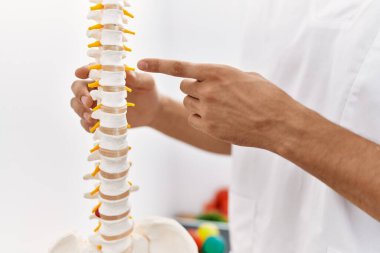 Fizyoterapist üniforması giyen genç Arap adam klinikte parmak omuza sütun gösteriyor.