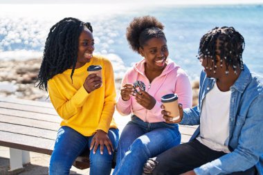 African american friends having breakfast sitting on bench at seaside