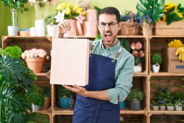 Handsome hispanic man working at florist shop angry and mad screaming frustrated and furious, shouting with anger. rage and aggressive concept. 