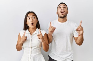 Soyutlanmış arka planda birbirine aşık genç ırklar arası bir çift şaşkınlık ve şaşkınlık içinde başlarını kaldırıp parmaklarıyla işaret ediyor ve kollarını kaldırıyordu.. 