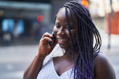 Afro-Amerikalı kadın gülümsüyor. Akıllı telefondan konuşuyor.