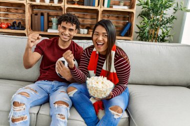 Evdeki kanepede oturan genç latin çift futbol maçını izliyor ve destekliyor..