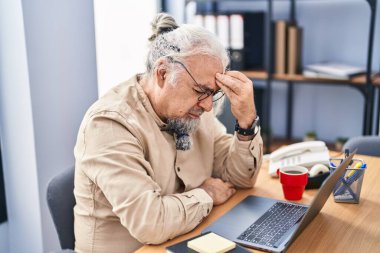 Orta yaşlı, kır saçlı, iş adamı. Ofiste dizüstü bilgisayar kullanıyor.