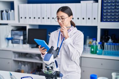 Young hispanic woman scientist using touchpad working at laboratory