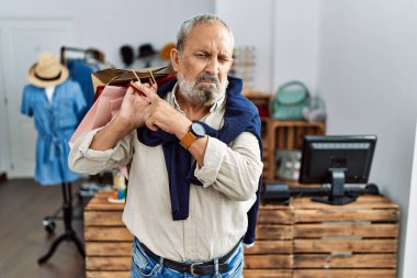 Butik dükkanında alışveriş torbaları tutan yakışıklı bir adam endişeli ve gergin bir kenara işaret ediyor işaret parmağı, endişeli ve şaşırmış ifade 