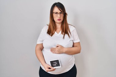 Pregnant woman holding baby ecography skeptic and nervous, frowning upset because of problem. negative person. 