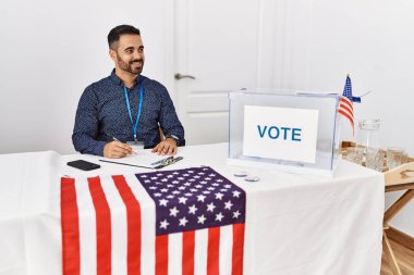 Young hispanic man smiling confident writing on clipboard working at electoral college