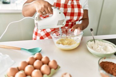 Hispanic brunette woman preparing cake with electric whisk at the kitchen