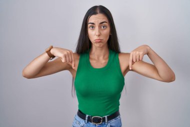 Young woman standing over isolated background pointing down looking sad and upset, indicating direction with fingers, unhappy and depressed. 