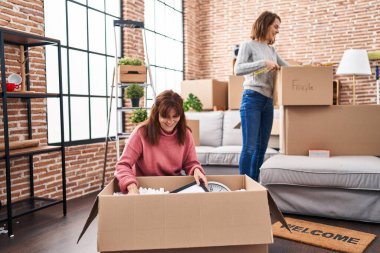 Two women mother and daughter unpacking cardboard box at new home