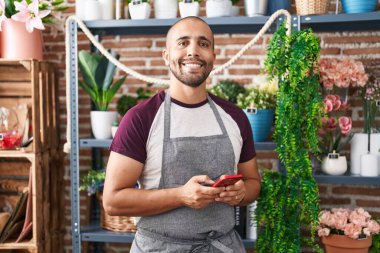Çiçekçide akıllı telefon kullanarak gülümseyen genç Latin bir çiçekçi.