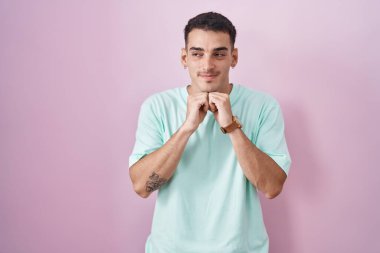 Yakışıklı İspanyol bir adam pembe arka planda duruyor. Gergin ve heyecanlı bir şekilde çene hizasına bakıyor. 
