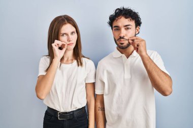 Gündelik kıyafetler giyen genç bir çift birbirine kenetlenmiş dudaklar ve ağızlar parmaklarla kapanmış fermuar gibi. gizli ve sessiz, tabu konuşması 
